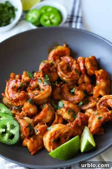 Gray bowl filled with bbq shrimp served with lime and jalapeño.