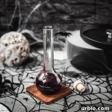 Glass bottle filled with berry blood Halloween syrup. Eerily beautiful, decorated with cobwebs and a black, steaming cauldron.