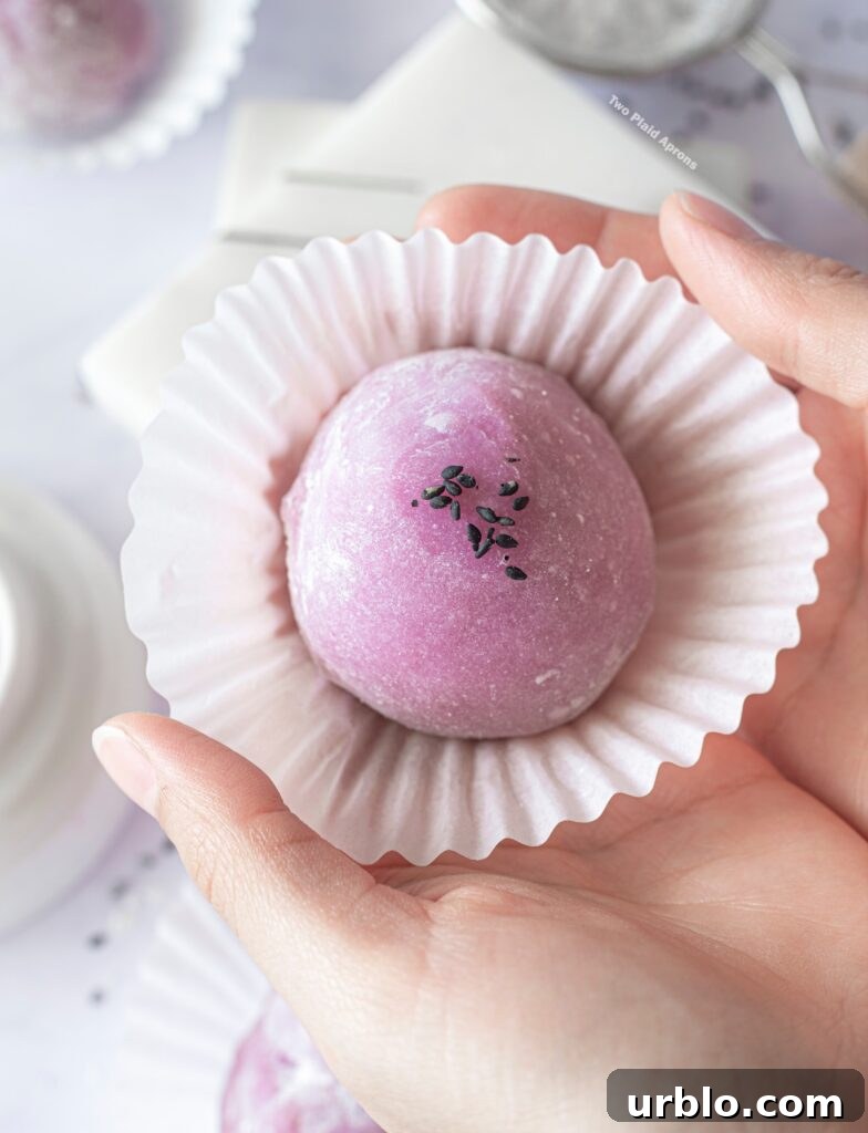 Holding an ube mochi with black sesame filling in a cupcake liner.
