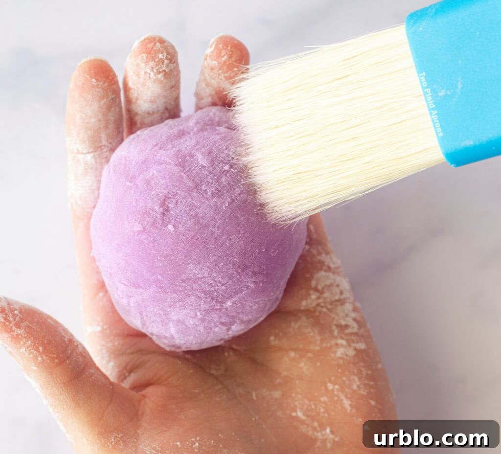 Brushing off excess cornstarch from the ube mochiwith a pastry brush.