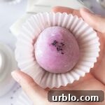 Holding an ube mochi with black sesame filling in a cupcake liner.