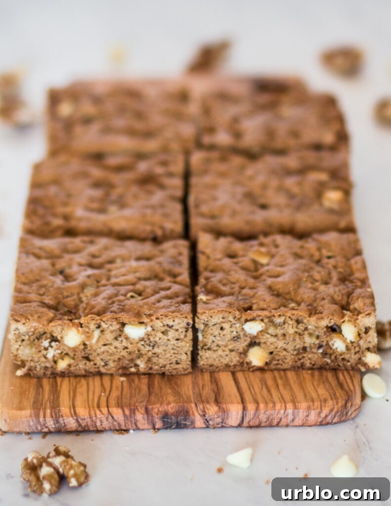 Gluten-Free White Chocolate Blondies Recipe — Chewy & Rich 3 gluten free white chocolate blondies cut into square bars and laid on a wooden cutting board