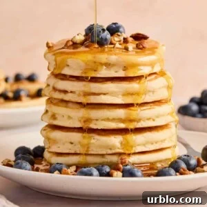 Stack of super fluffy pancakes on plate with blueberries, pecans, and maple syrup.