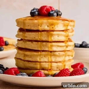 Stack of pancakes topped with berries and maple syrup being poured from above.
