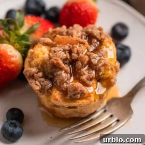 Baked French toast muffin with streusel topping on plate with maple syrup poured over top.