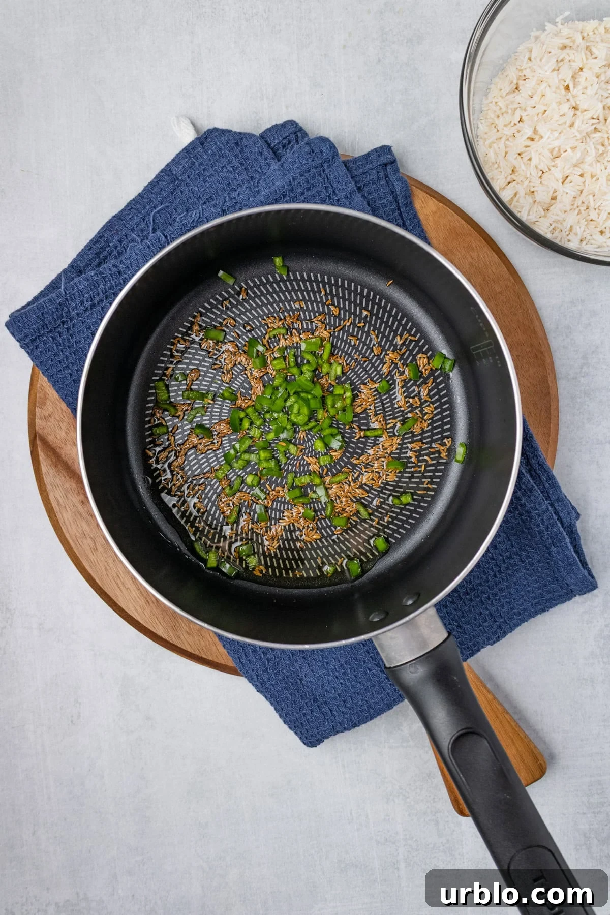 An overhead image of cooking cumin seeds and chopped green chili in a skillet.
