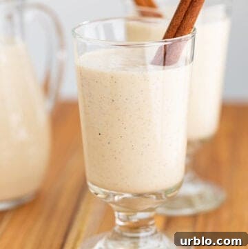 glass of eggnog with a cinnamon stick on a wooden surface