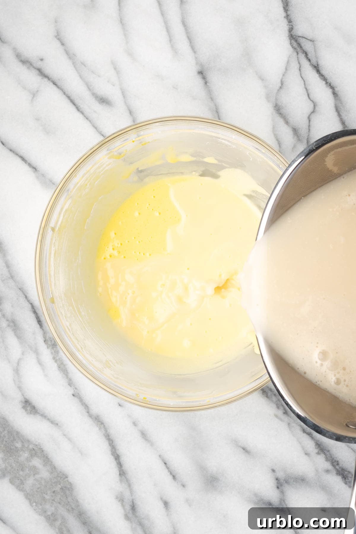 Hot milk being slowly added to the egg yolk mixture.