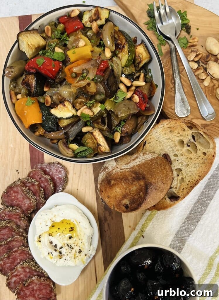 Styled overhead photo of vegetable caponata and other antipasto foods (cheeses, salami, olives, bread).