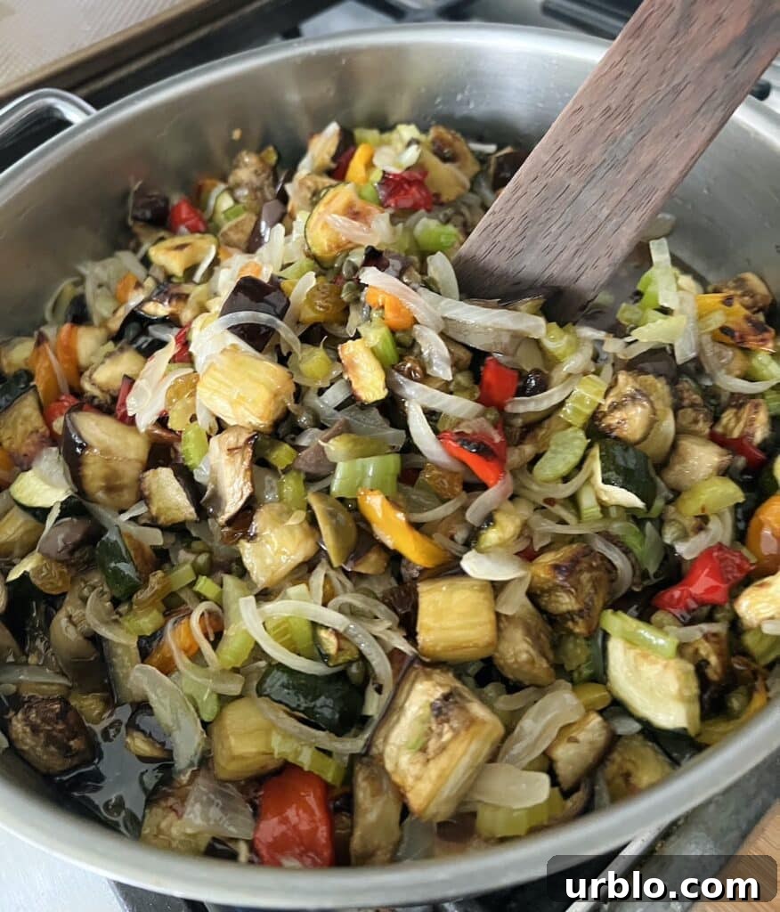 Vegetable caponata mixture in pan with wooden spoon.