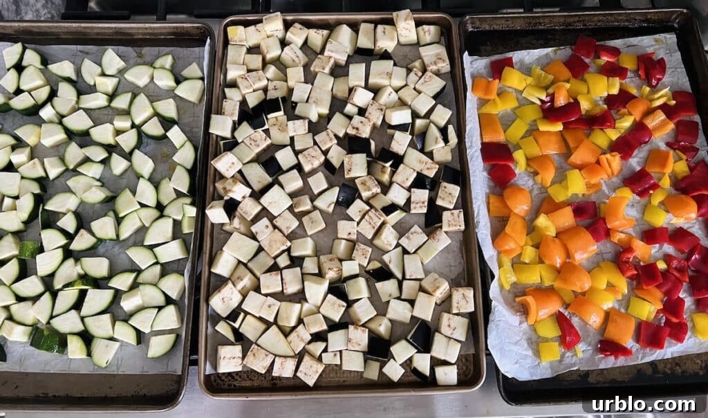 Zucchini, eggplant and bell peppers on separate parchment-lined sheet pans.