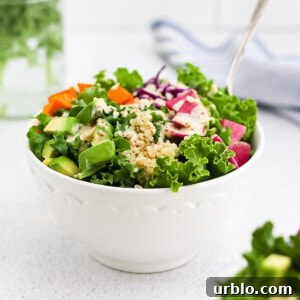 A white bowl holding a power bowl consisting of kale, quinoa, avocado, sweet potato, radishes, cabbage, and a tahini dressing on top.
