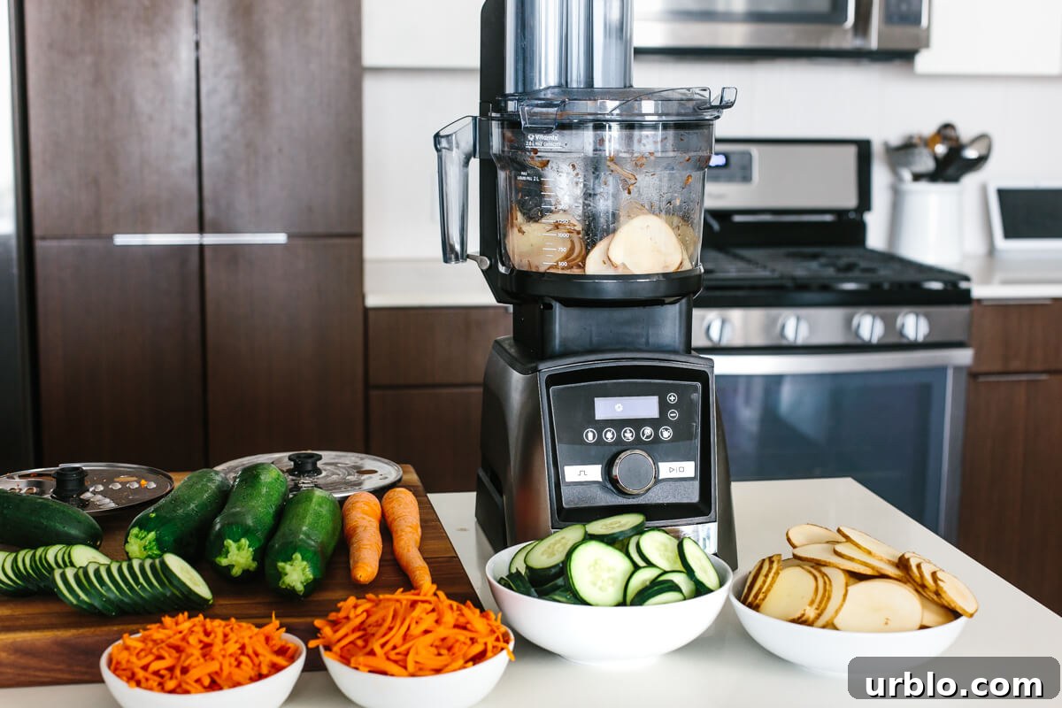 Bowls of sliced and shredded vegetables in front of the Vitamix food processor.