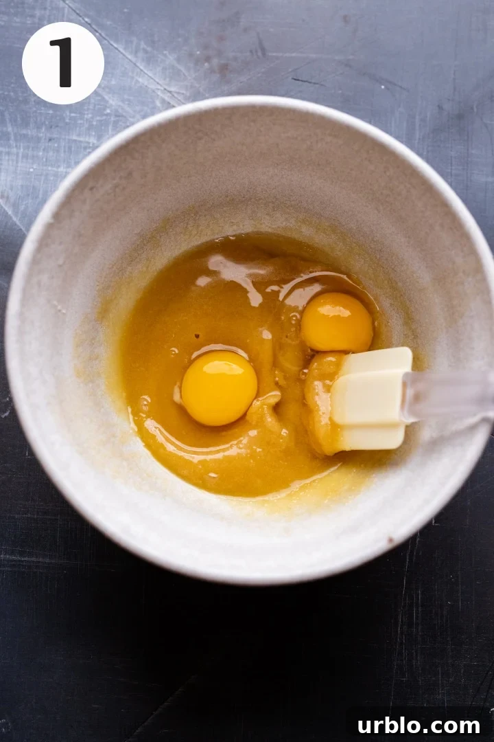 Step 1 - a ceramic white bowl with eggs and creamed butter and sugar in it on a gray background.