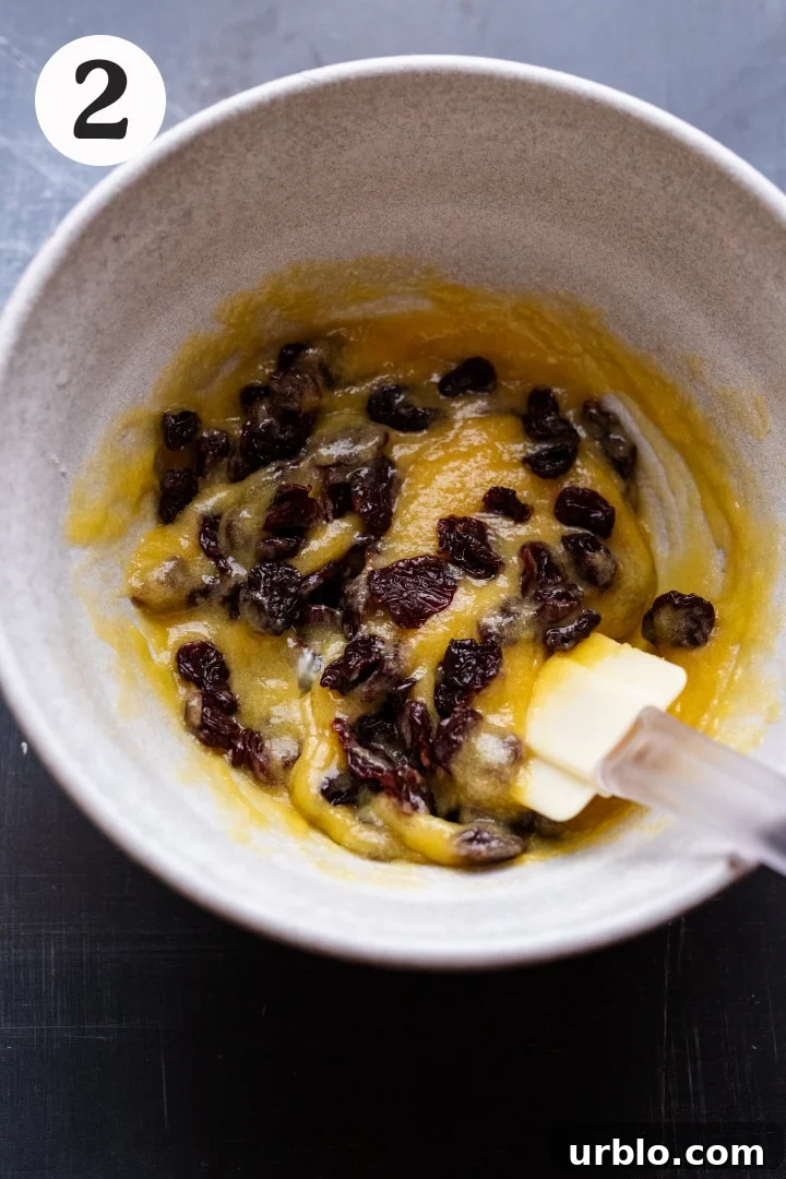 A white ceramic bowl with creamed butter and sugar and dried cherries in it on a gray background.