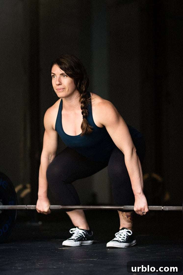 white woman with brown hair dressed in tank top and black pants doing a barbell deadlift