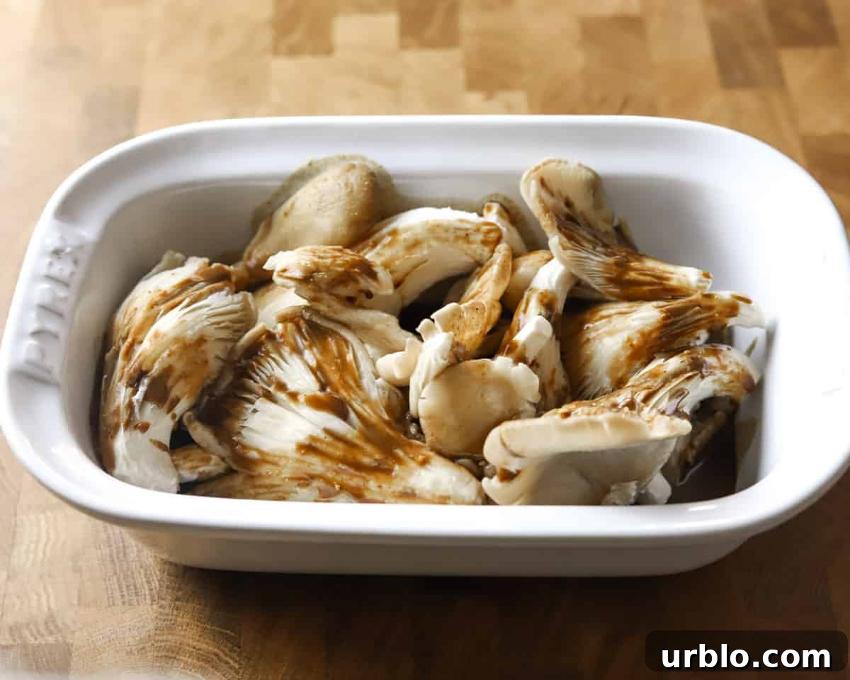 Photo showing oyster mushrooms and marinade mixture poured over them, in a white dish on a wooden tabletop.
