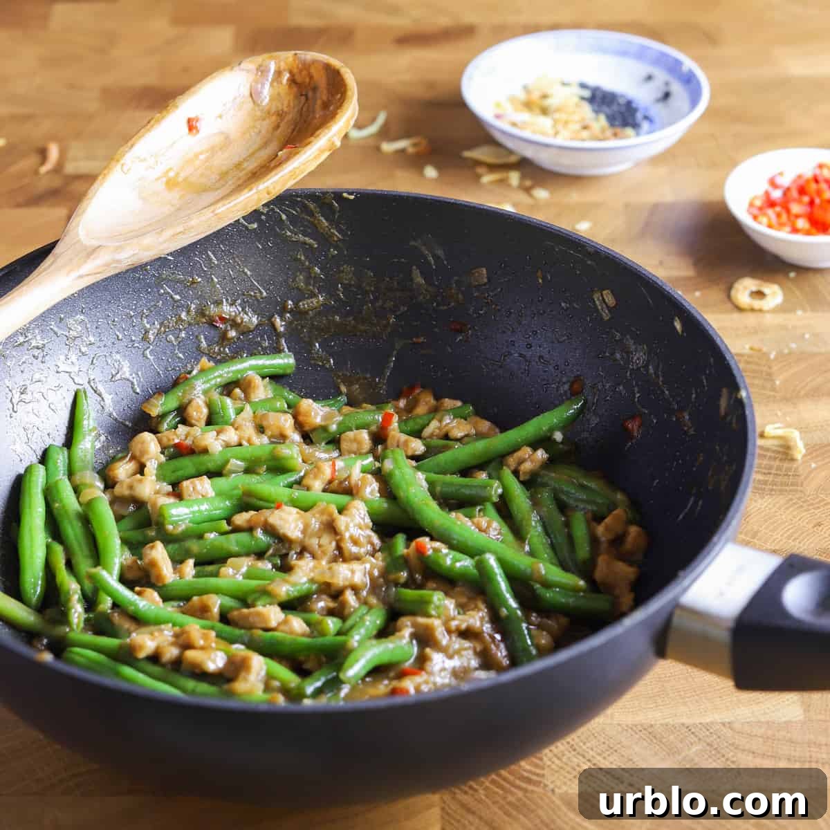 photo of a wok containing vegan chinese green beans and tempeh recipe on a butcher block surface
