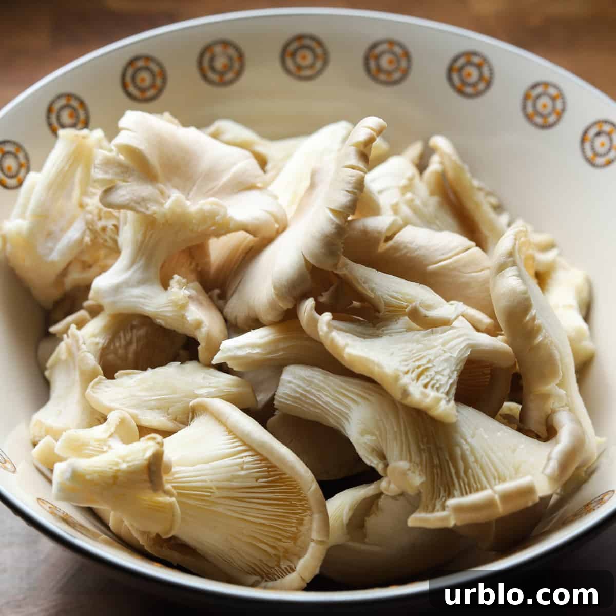 Photo showing a bowl of raw pearl oyster mushrooms on a wooden tabletop.