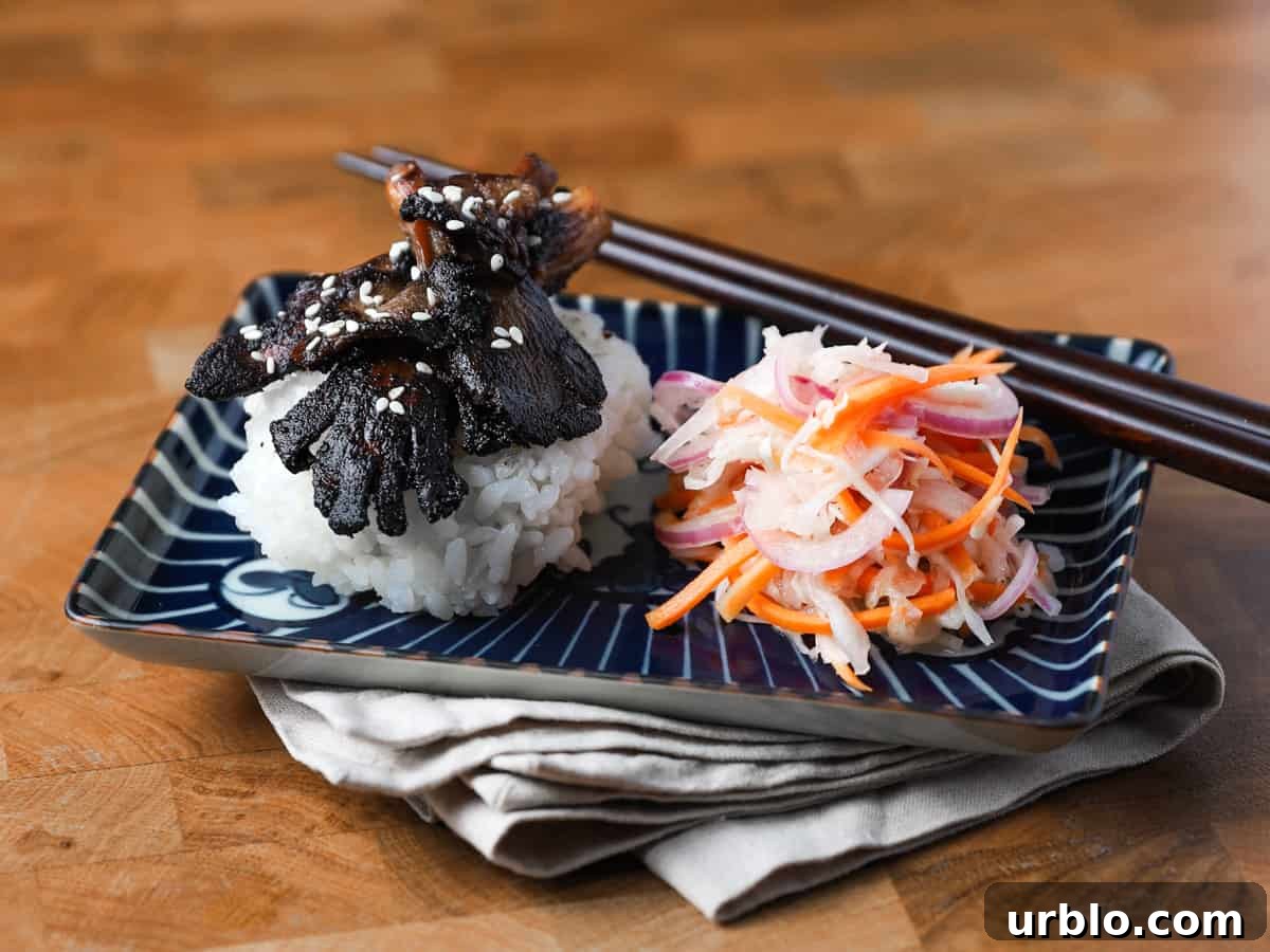 Photo of a dark blue patterned oblong dish resting on a napkin on a wooden table with Char Siu mushrooms, sushi rice and pickled salad.