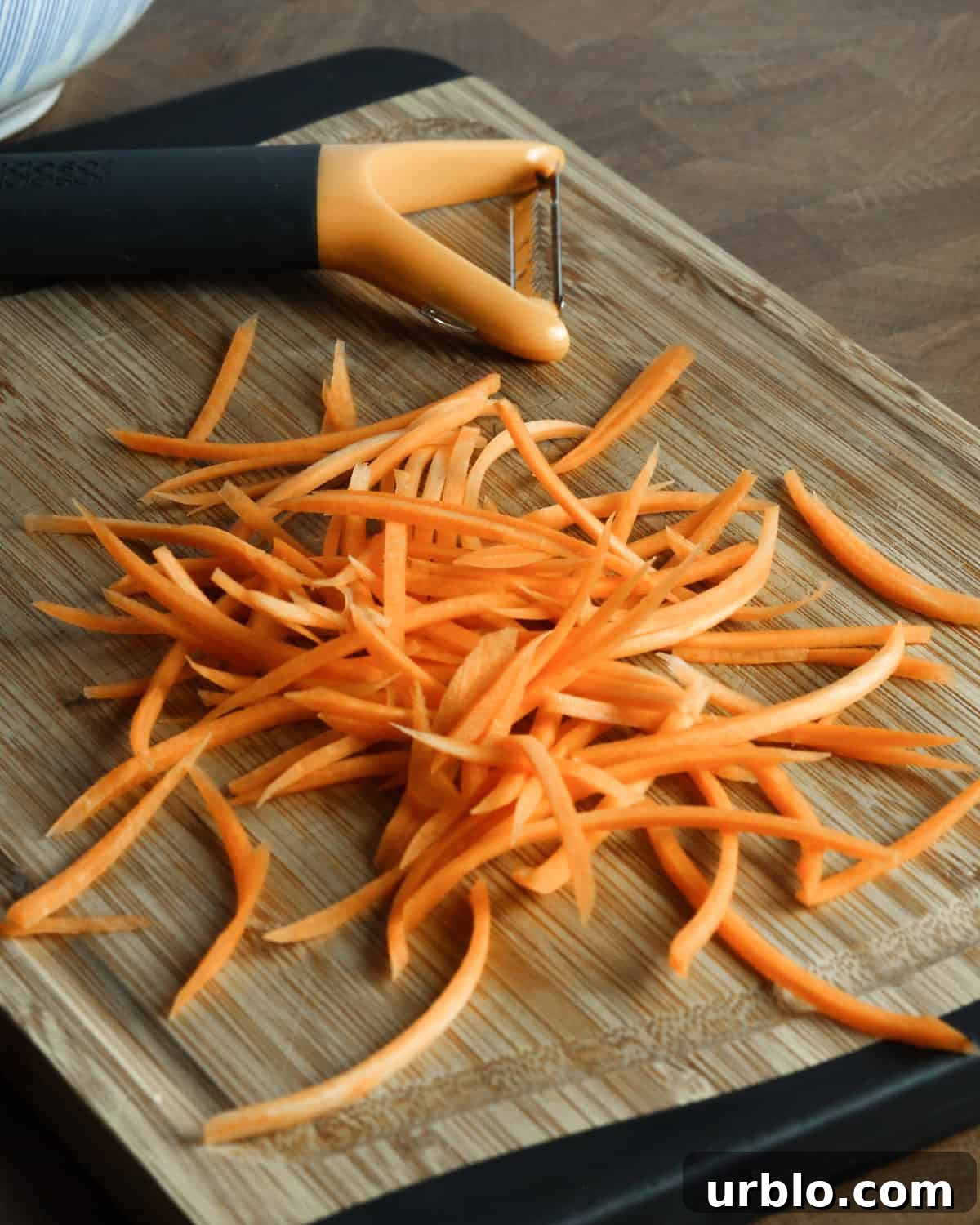Photo of julienned carrot on a chopping board with a Y-shaped julienne peeler.