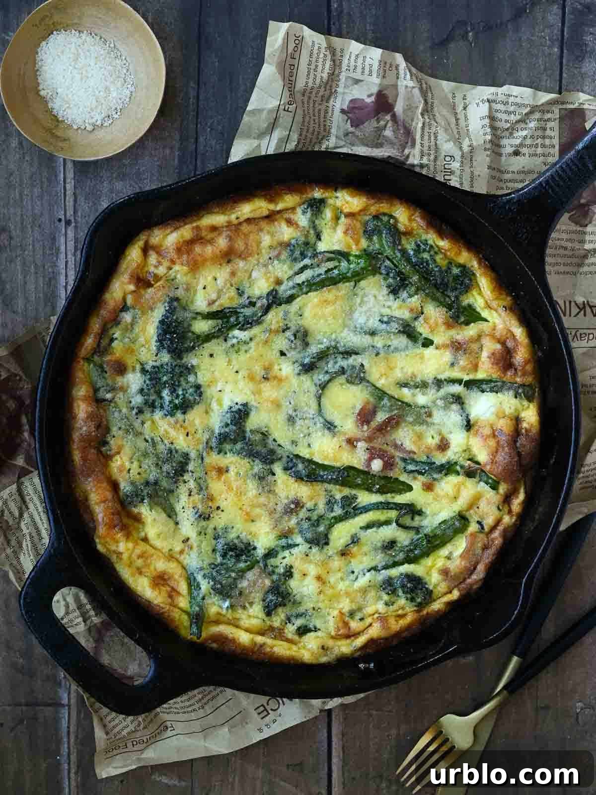 Overhead view of broccolini frittata in a black skillet on a wooden surface.