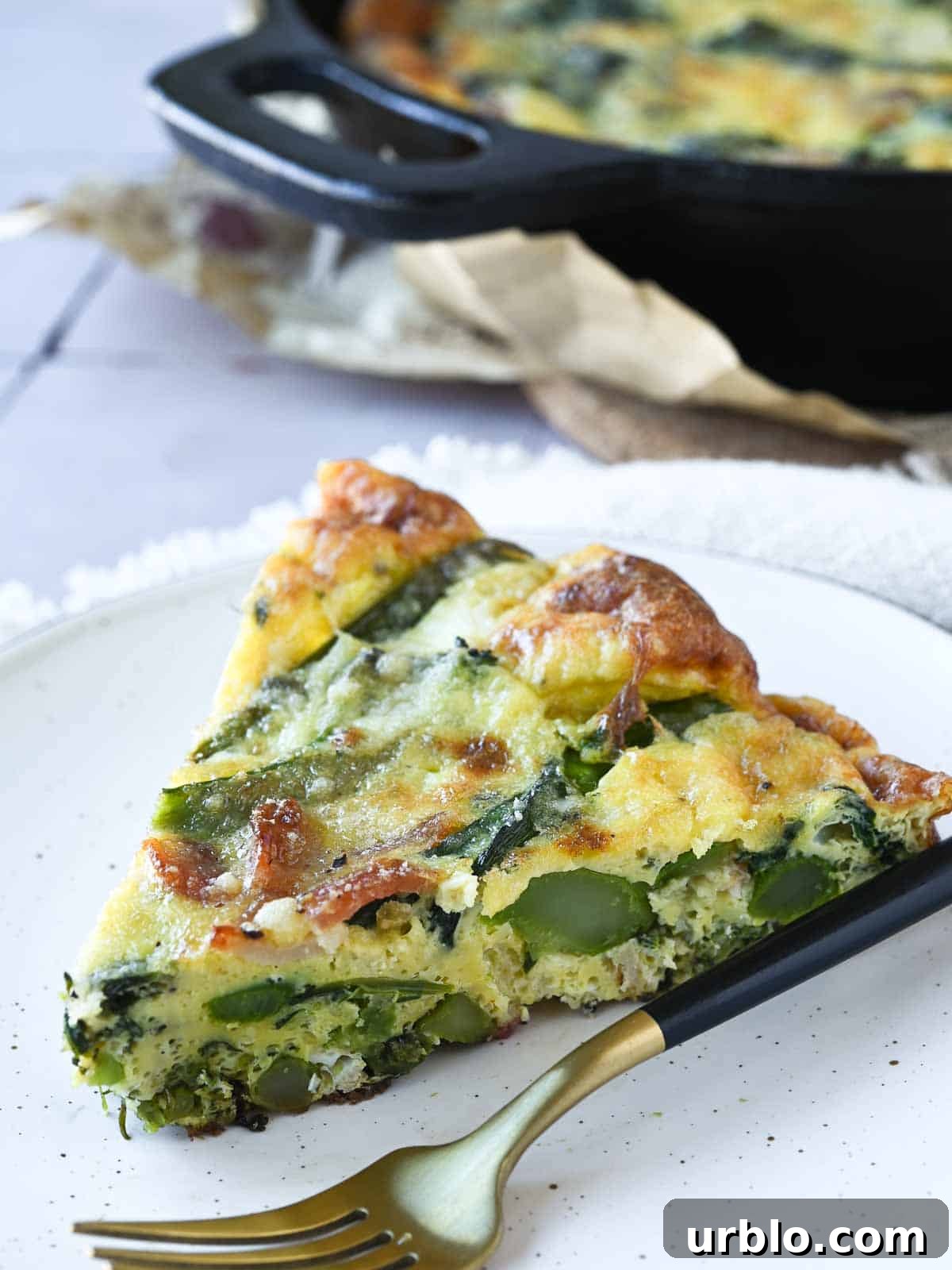 A slice of broccolini frittata on a beige plate with a fork next to it.