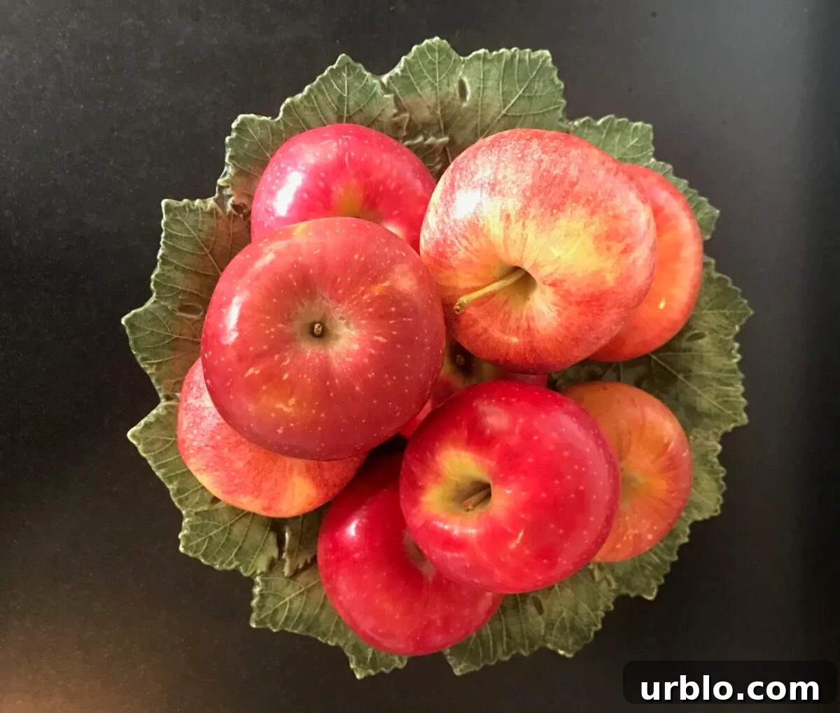 Green leafy ceramic pedestal dish with an assortment of fresh apples on top.