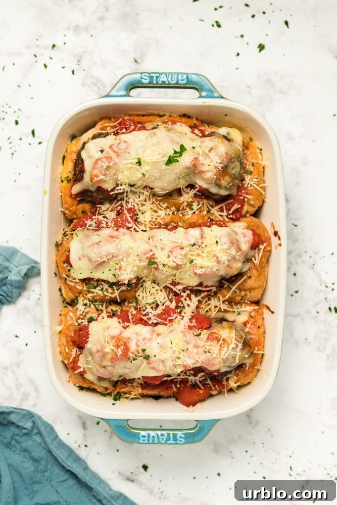 A baking dish filled with stuffed rolls, resembling meatball sub boats.