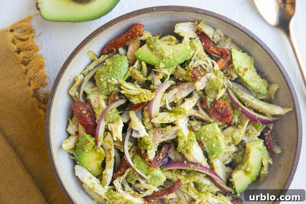 large serving bowl of chicken pesto salad with a golden napkin to the side and a gold spoon.