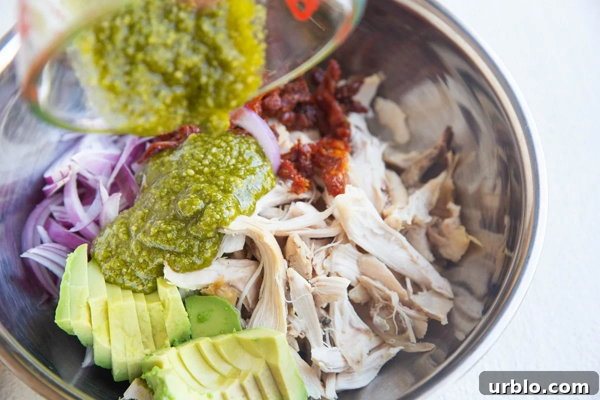 Pouring pesto sauce over the chicken salad ingredients.