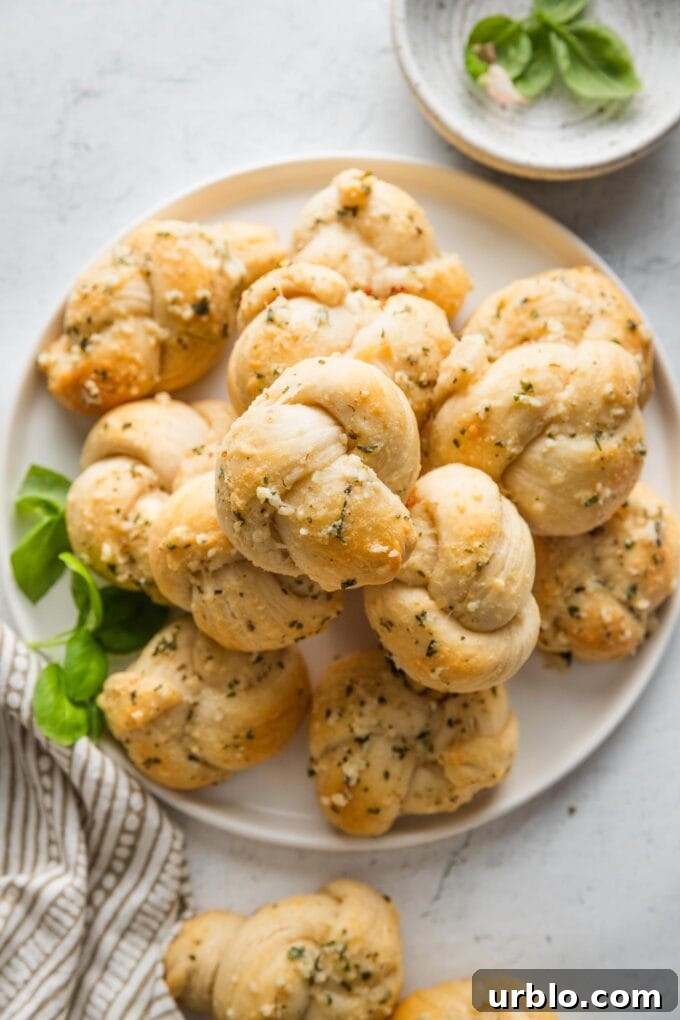 Small white plate piled high with garlic Parmesan biscuit garlic knots with fresh basil scattered nearby.