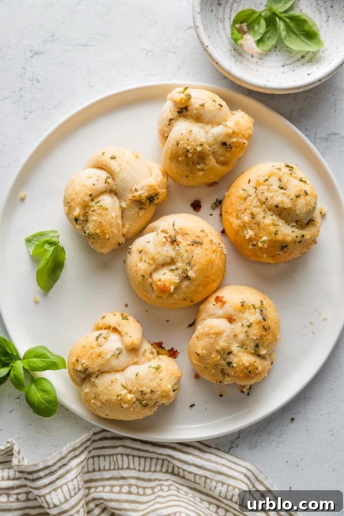 Countertop set with a small plate of garlic knots made out of biscuit dough, a patterned napkin, and extra basil leaves.