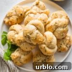 Small white plate piled high with garlic Parmesan biscuit garlic knots with fresh basil scattered nearby.
