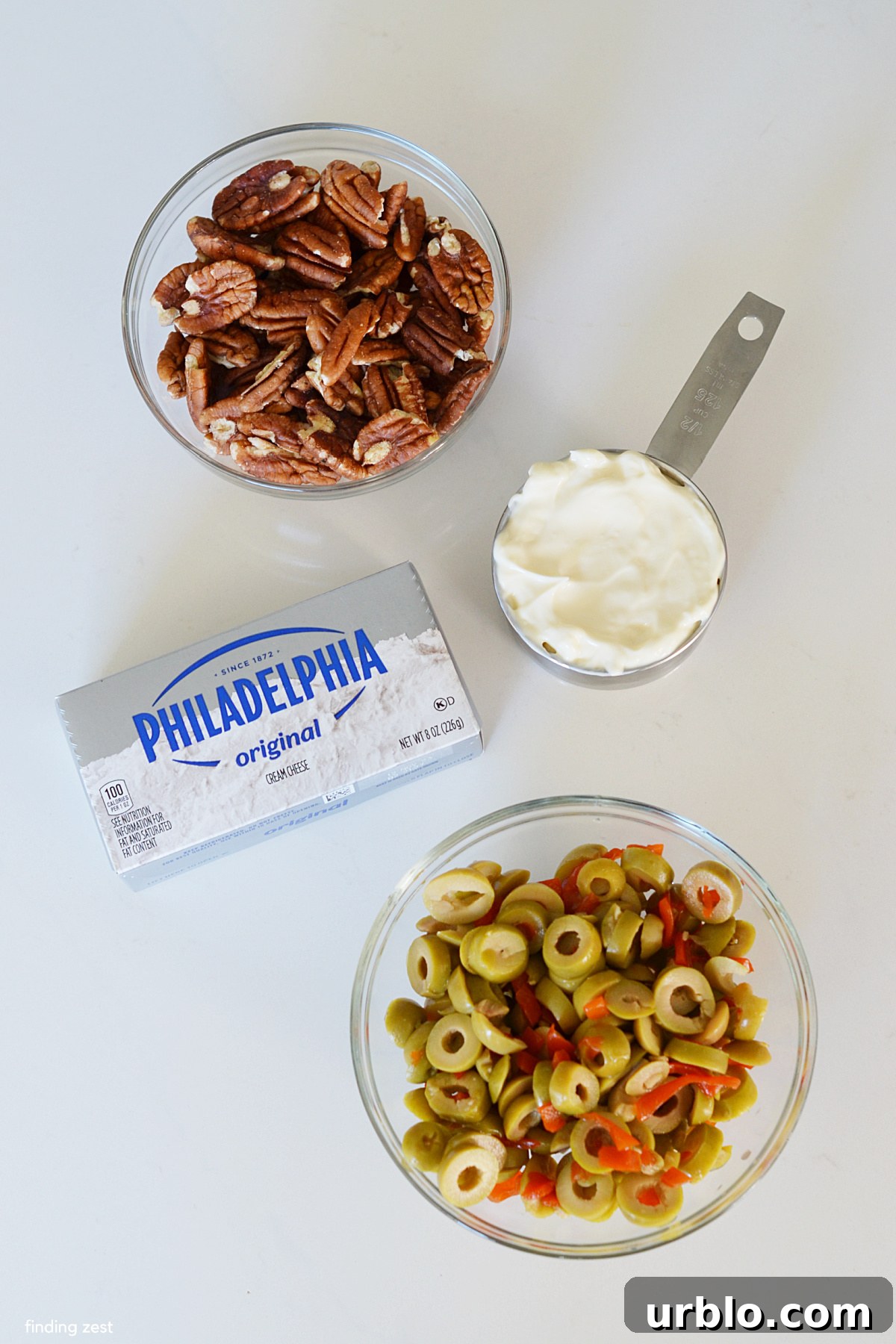 Ingredients for an olive dip including cream cheese, mayo, sliced green olives and chopped pecans.