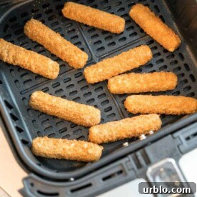 Crispy Air Fryer Frozen Mozzarella Sticks in 10 Minutes 3 Frozen mozzarella sticks are neatly arranged in an air fryer basket, ready to be cooked.