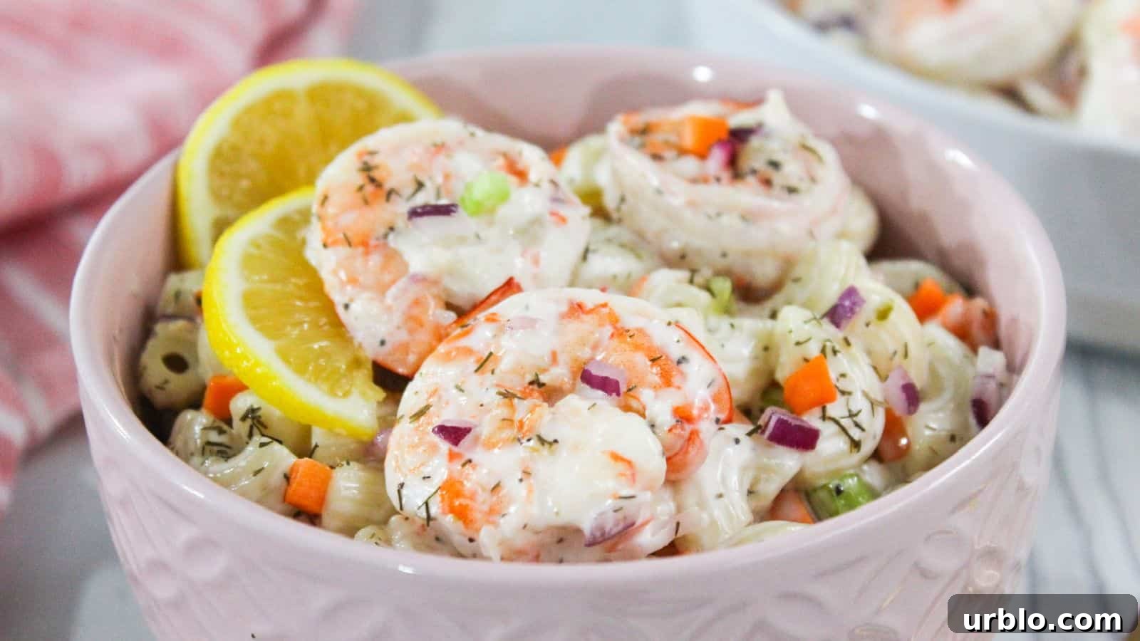 Shrimp macaroni salad in a pink bowl with lemon wedges.