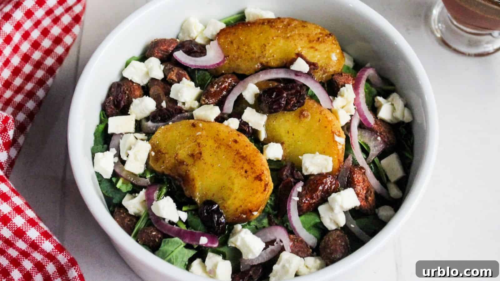 A bowl of salad with mixed greens, air-fried apples, red onions, nuts, and crumbled cheese.