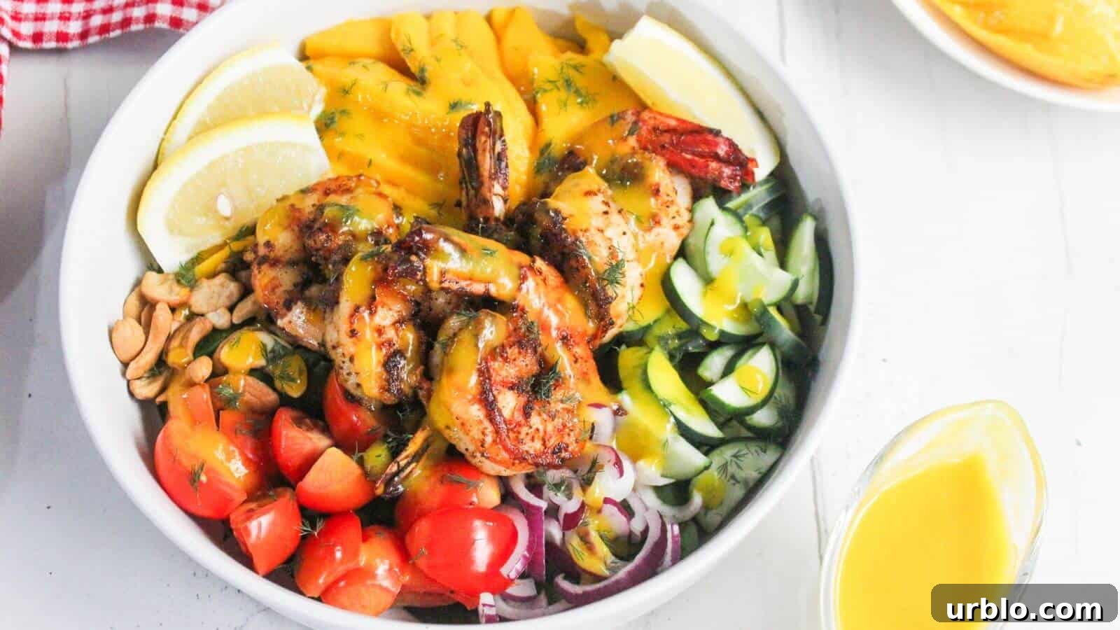 A bowl with grilled shrimp, sliced mango, lemon wedges, cherry tomatoes, cucumbers, red onions, peanuts, and greens, topped with a yellow sauce.