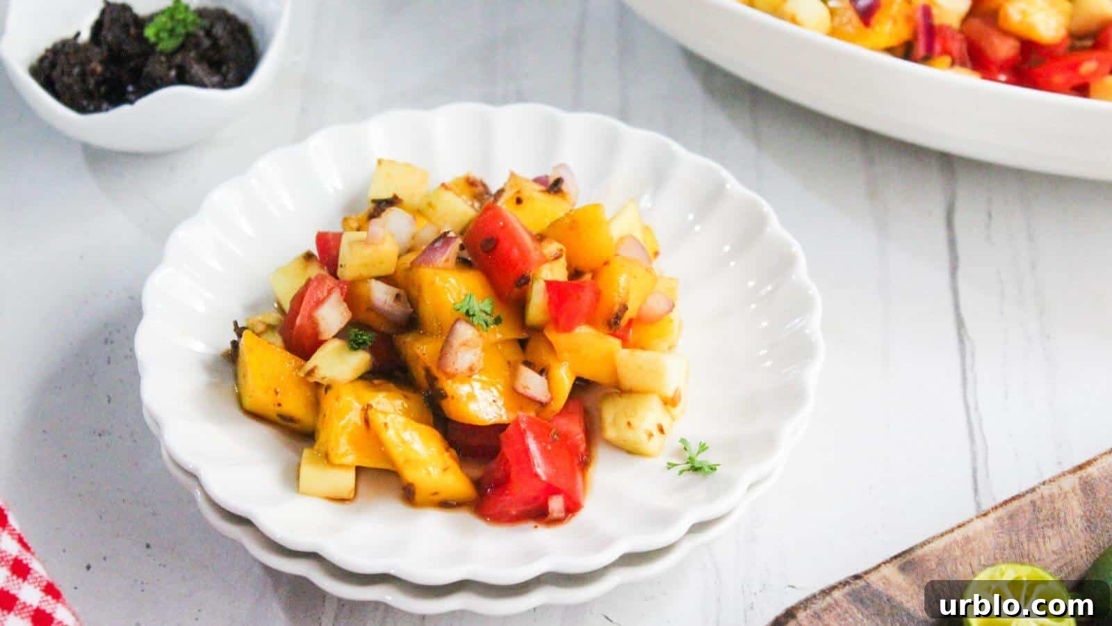 A white plate with a mixed fruit and vegetable salad, including mango, apple, red bell pepper, and onions, garnished with herbs.