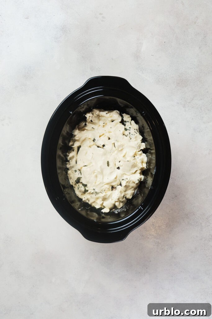 Cream cheese over chicken in a black crock pot.