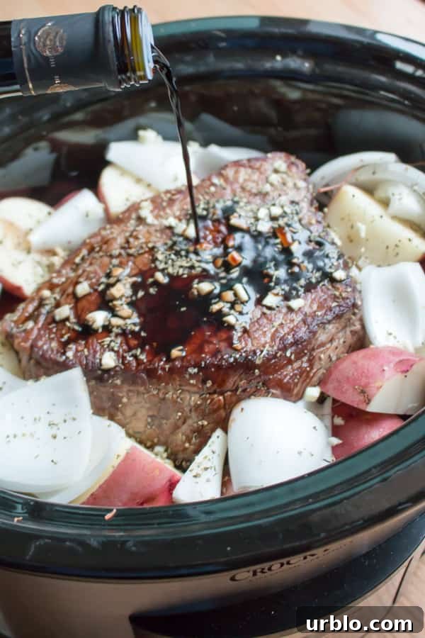 Balsamic vinegar being pour over beef roast, garlic and vegetables in slow cooker.