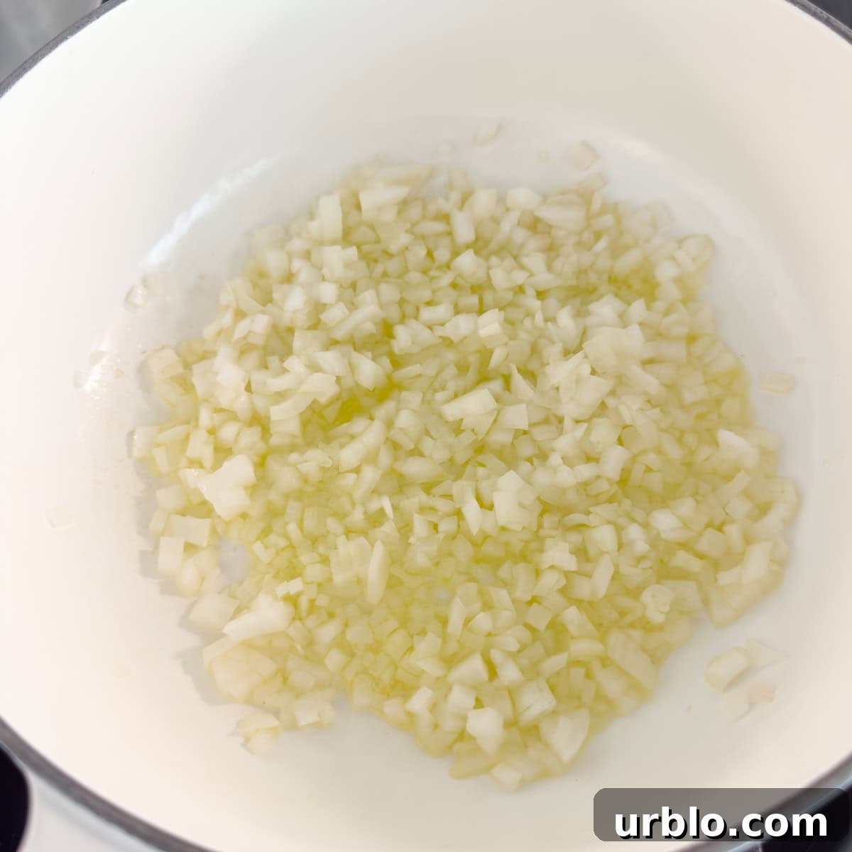 Sautéing chopped white onion in olive oil in a white dutch oven.