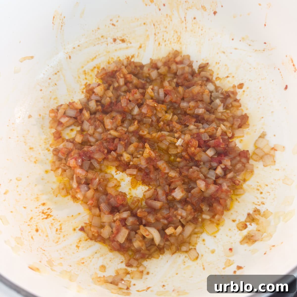 Tomato paste stirred into white rice turning it red in a pot.