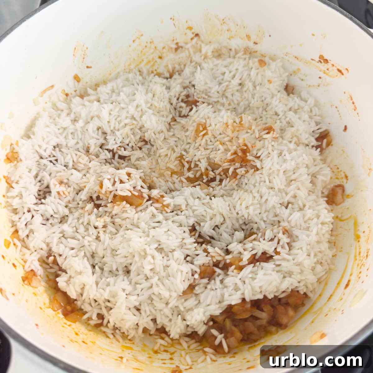 White rice added to a pot of cooking onions and spices.