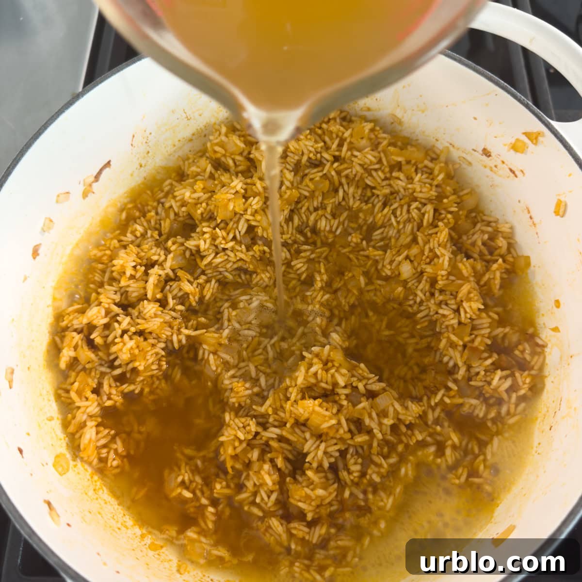Golden broth pouring into a pot of cooking rice in a havey pot.