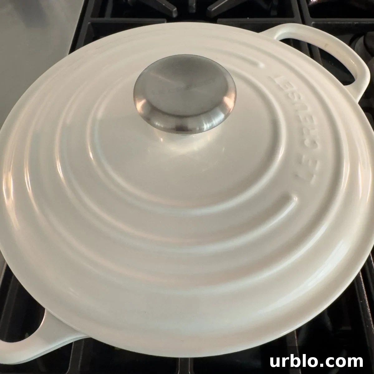 A white dutch oven with a silver top handle with the lid on the stove.