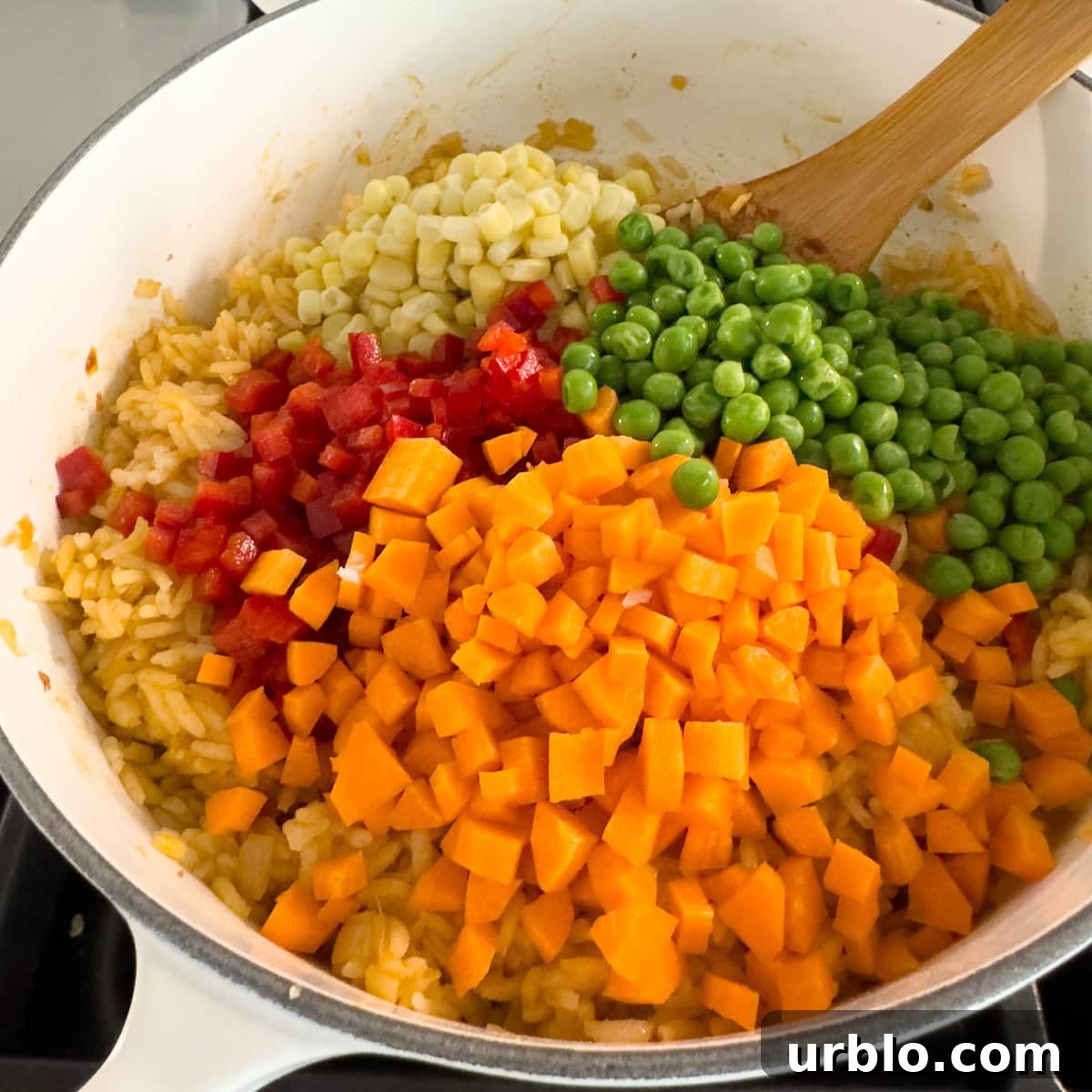 Carrots, bell peppers, peas, and corn added to a pot of rice.