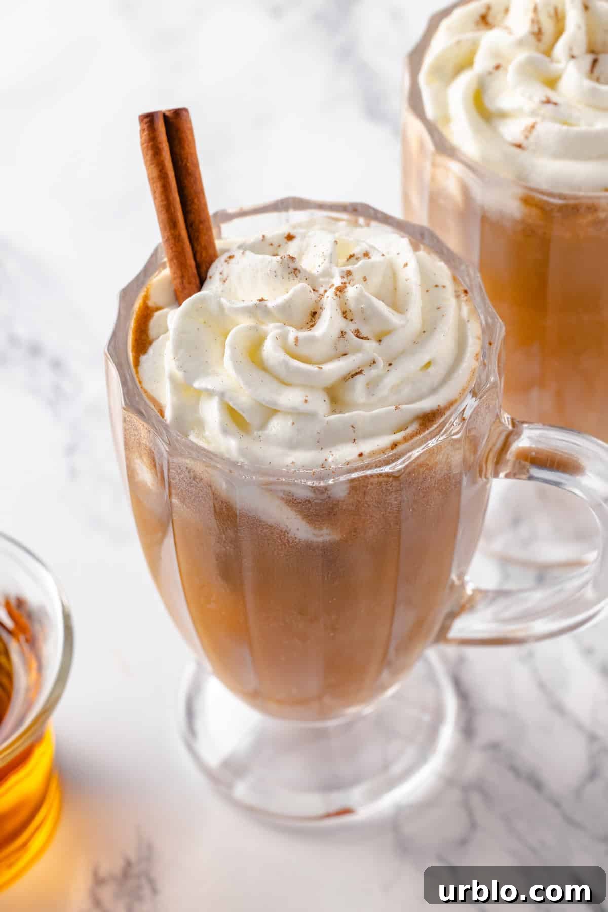 Glass mug of hot buttered rum with whipped cream and cinnamon stick