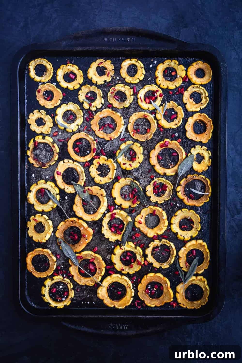 Sliced roasted squash rings on baking sheet, can see entire sheet, topped with fresh sage leaves. Pre Oven.